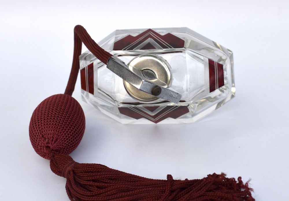 An Art Deco cut crystal perfume atomiser featuring burgundy geometric chevron detailing, chrome fittings, and a matching burgundy squeeze bulb with a long tassel. View IV