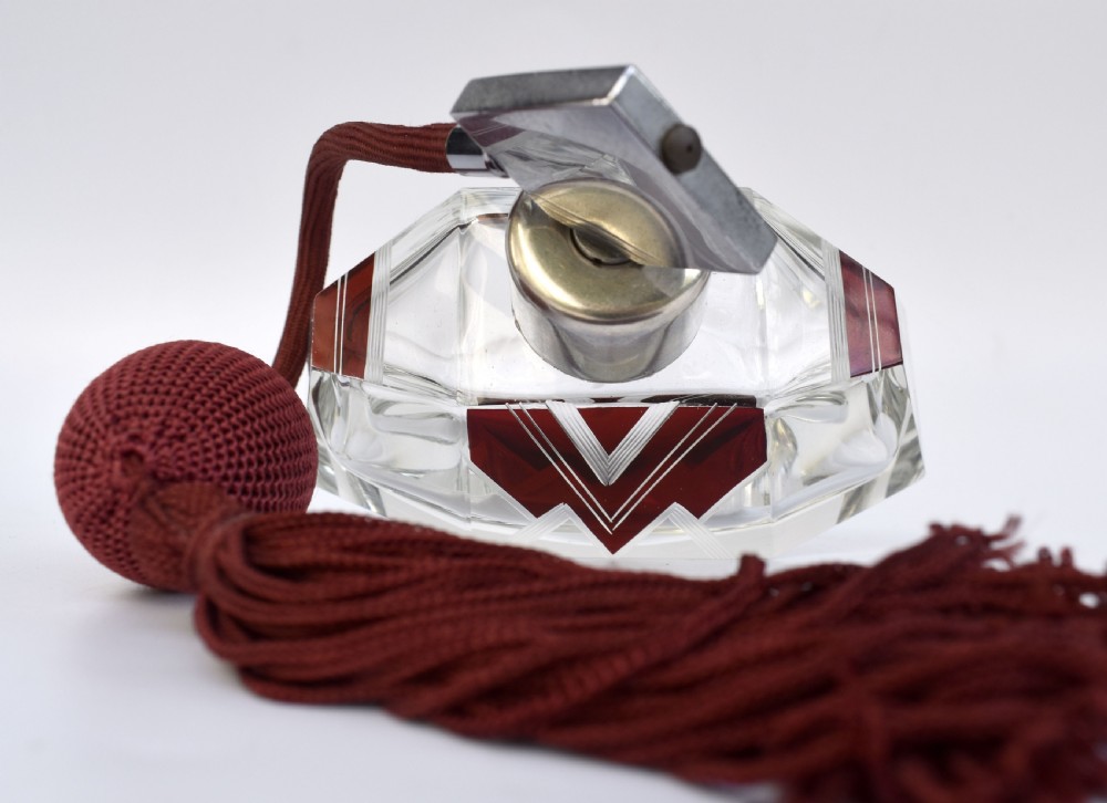 An Art Deco cut crystal perfume atomiser featuring burgundy geometric chevron detailing, chrome fittings, and a matching burgundy squeeze bulb with a long tassel. View V