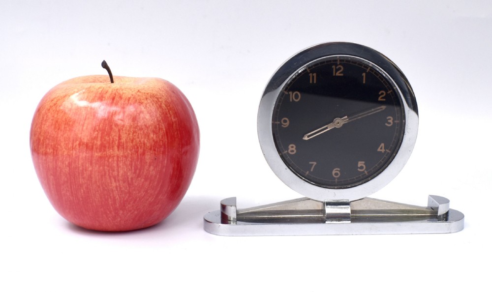 A circular Art Deco desk clock featuring a black dial with gold numerals, mounted on a geometric polished chrome base. View VIII