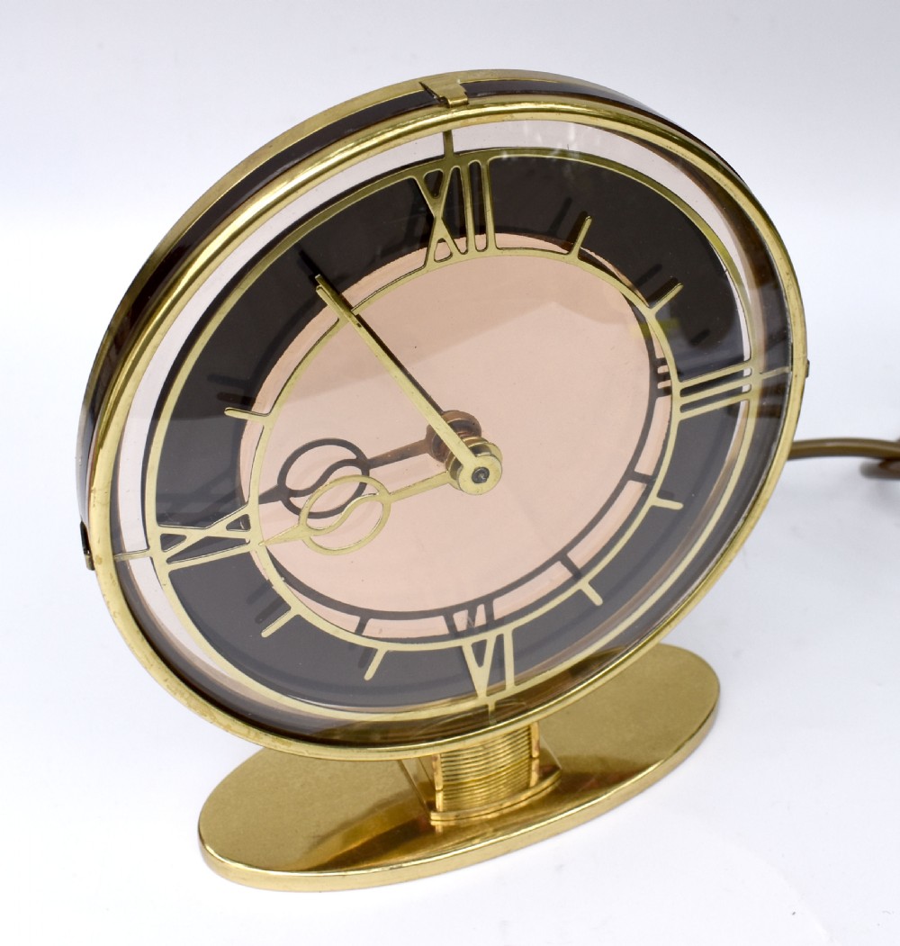 A circular Art Deco brass mantel clock with a pink mirrored dial, Roman numerals, and an oval brass base. View II