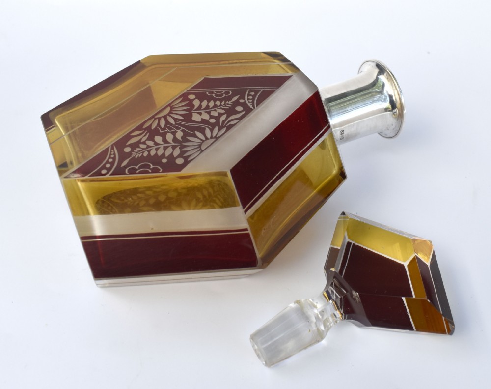 An Art Deco geometric glass decanter with a diamond-shaped stopper surrounded by six matching glass tumblers featuring amber glass and red floral etched panels. View II