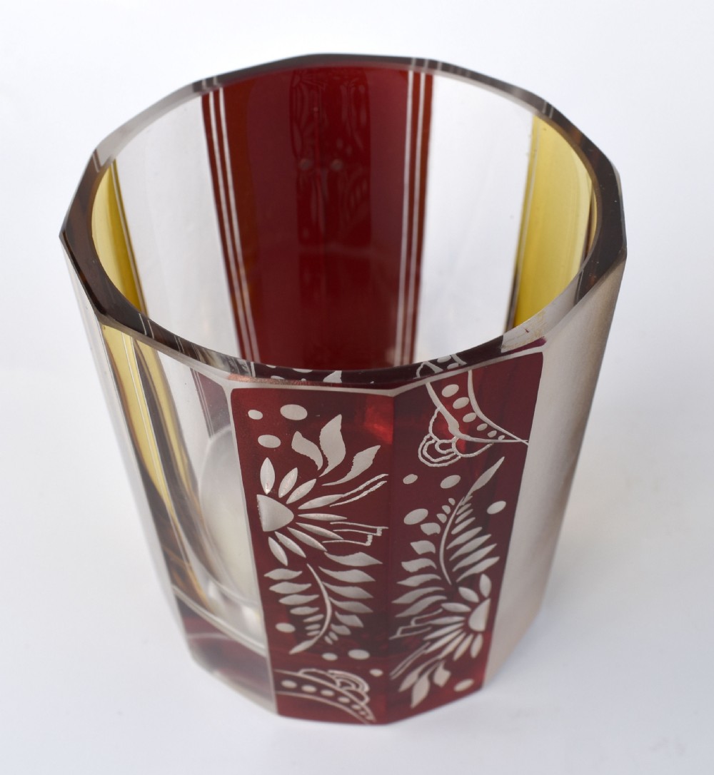 An Art Deco geometric glass decanter with a diamond-shaped stopper surrounded by six matching glass tumblers featuring amber glass and red floral etched panels. View VII