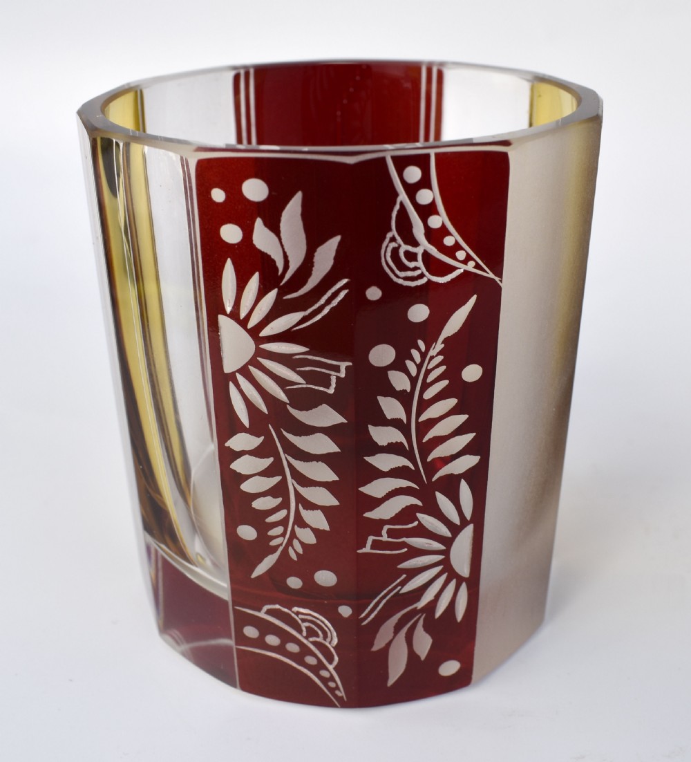 An Art Deco geometric glass decanter with a diamond-shaped stopper surrounded by six matching glass tumblers featuring amber glass and red floral etched panels. View VIII