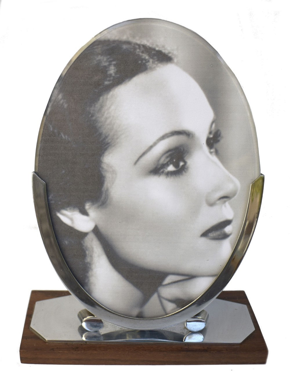 An Art Deco oval chrome photo frame supported by two curved metal brackets on a chrome and dark wood plinth base.