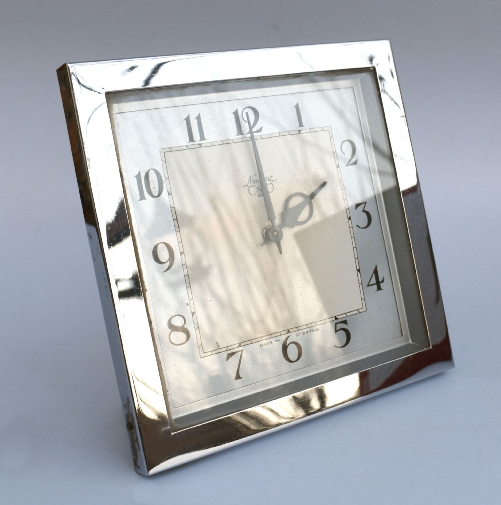 A square Art Deco chrome desk clock featuring a two-tone dial with black Arabic numerals and stylised hands. View VI