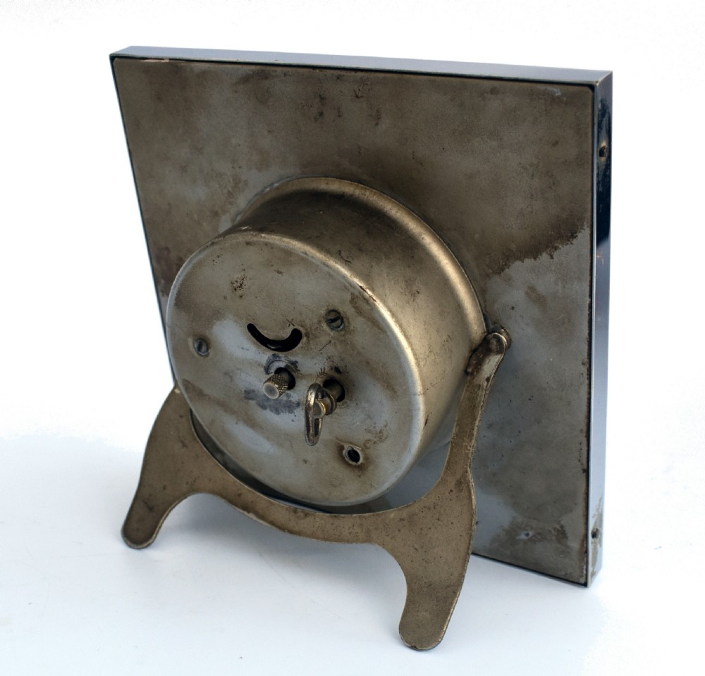 A square Art Deco chrome desk clock featuring a two-tone dial with black Arabic numerals and stylised hands. View VII
