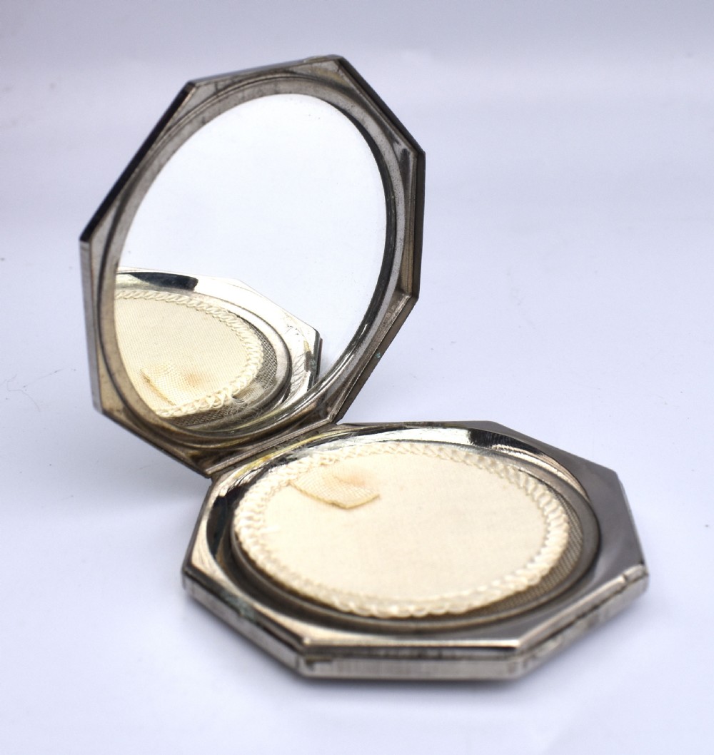 An octagonal Art Deco powder compact featuring terracotta red enamelled side panels and a central faux snakeskin section bordered by brass trim. View II