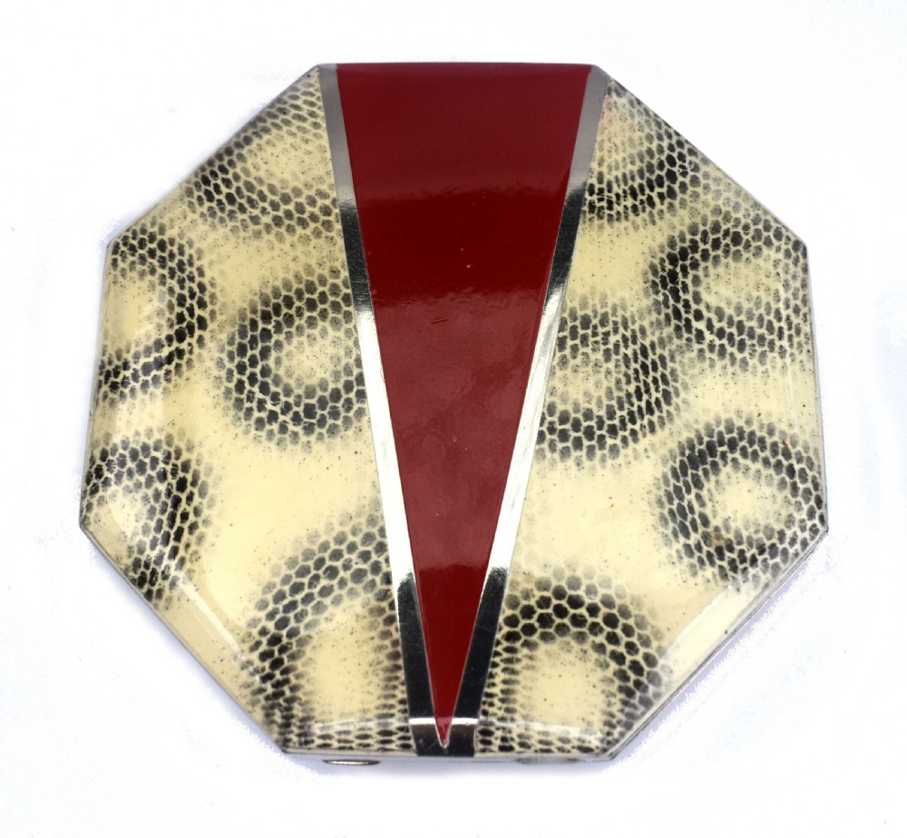 An octagonal Art Deco powder compact featuring a central red enamel chevron motif framed by a cream and black patterned ground.