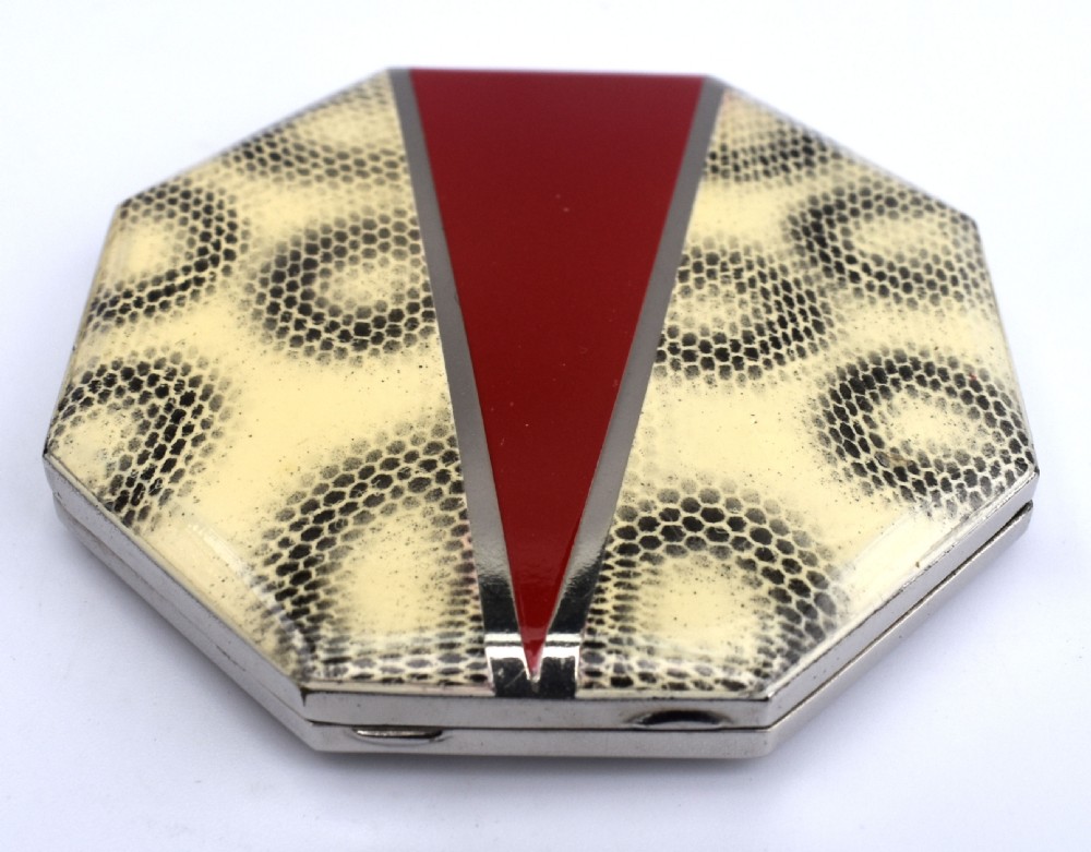 An octagonal Art Deco powder compact featuring a central red enamel chevron motif framed by a cream and black patterned ground. View V
