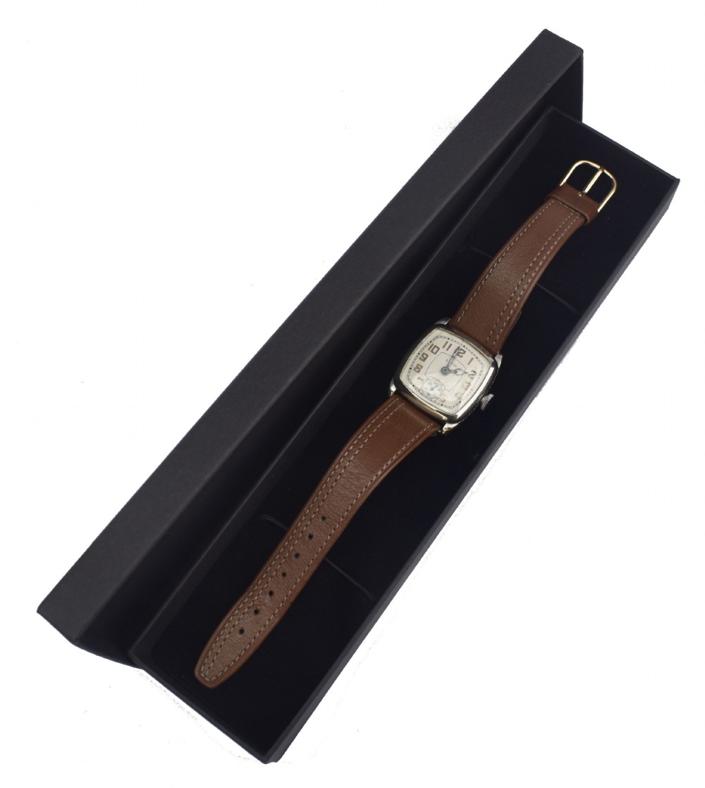 An Art Deco Elgin gentlemans wrist watch featuring a cushion-shaped 14k white gold case, cream dial with black Arabic numerals, small seconds dial, and a stitched brown leather strap. View VI