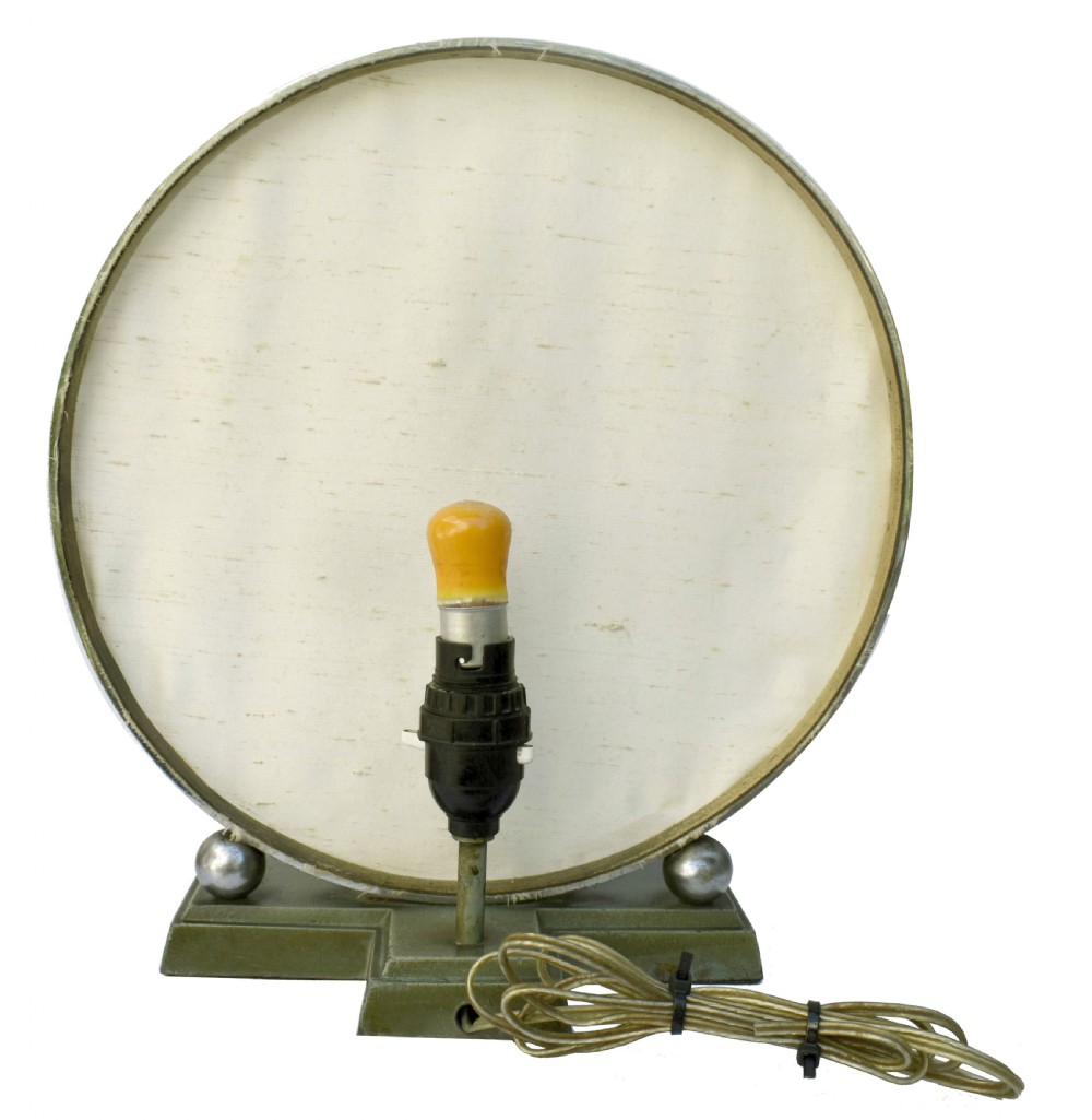 An Art Deco style table lamp featuring a green patinated metal female tennis player figurine standing in front of a circular cream fabric backdrop on a stepped base. View III