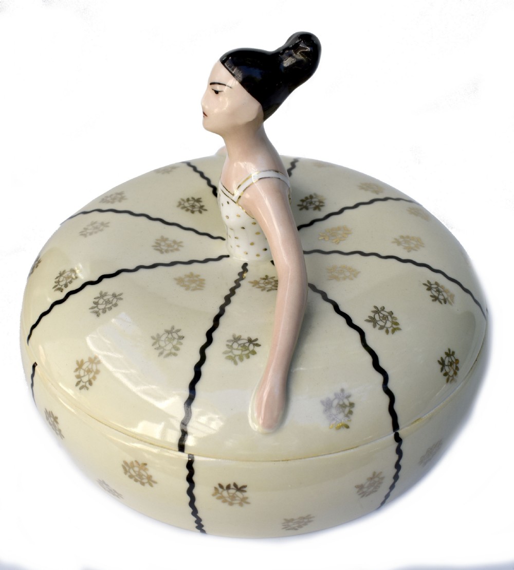 An Art Deco cream ceramic powder bowl with a lid sculpted in the form of a woman wearing a gown decorated with dark vertical wavy stripes and gilt floral motifs. View II