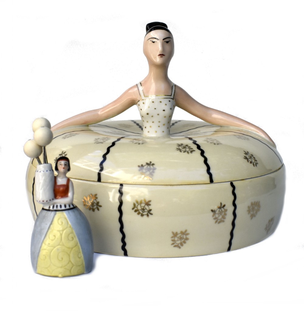 An Art Deco cream ceramic powder bowl with a lid sculpted in the form of a woman wearing a gown decorated with dark vertical wavy stripes and gilt floral motifs. View III