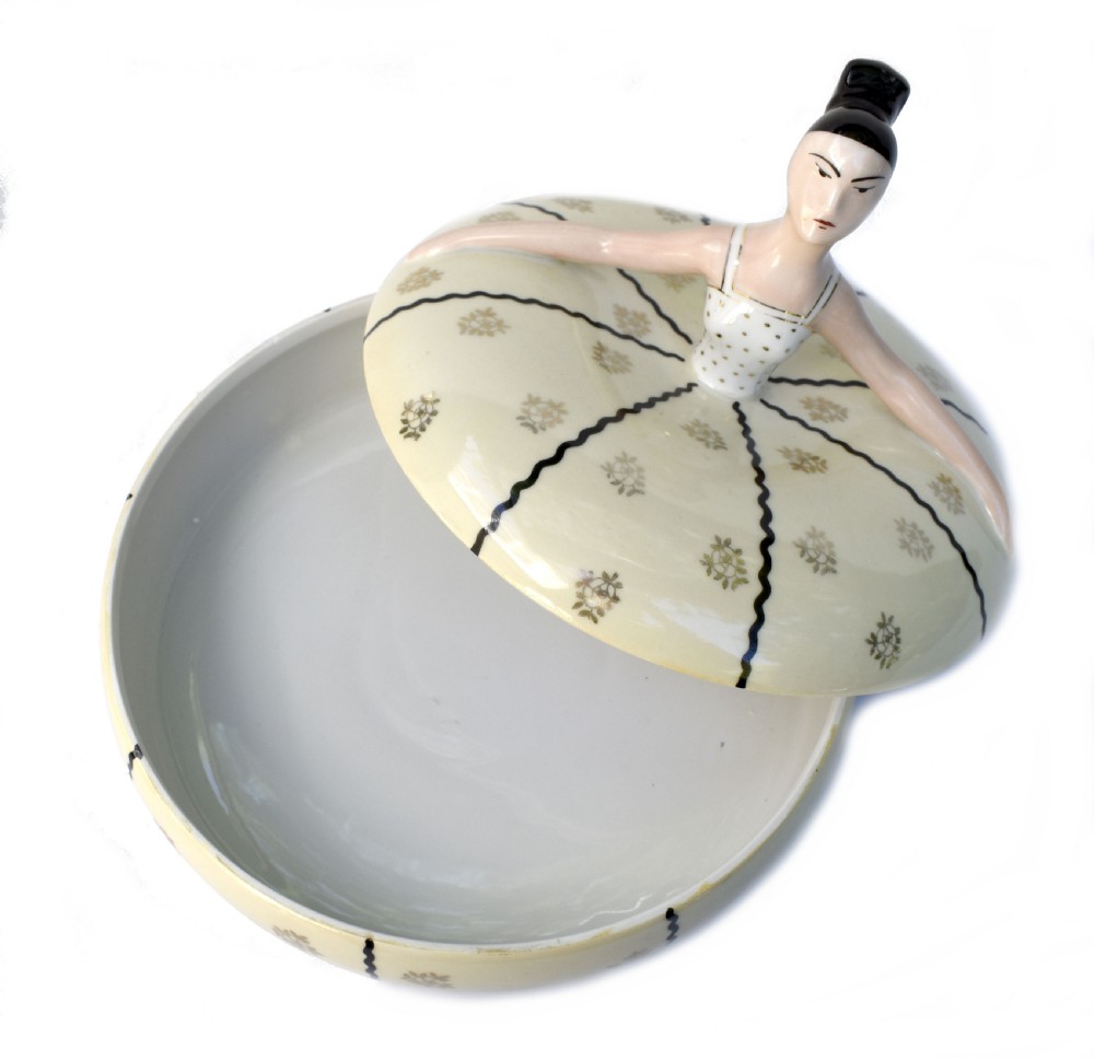 An Art Deco cream ceramic powder bowl with a lid sculpted in the form of a woman wearing a gown decorated with dark vertical wavy stripes and gilt floral motifs. View IV