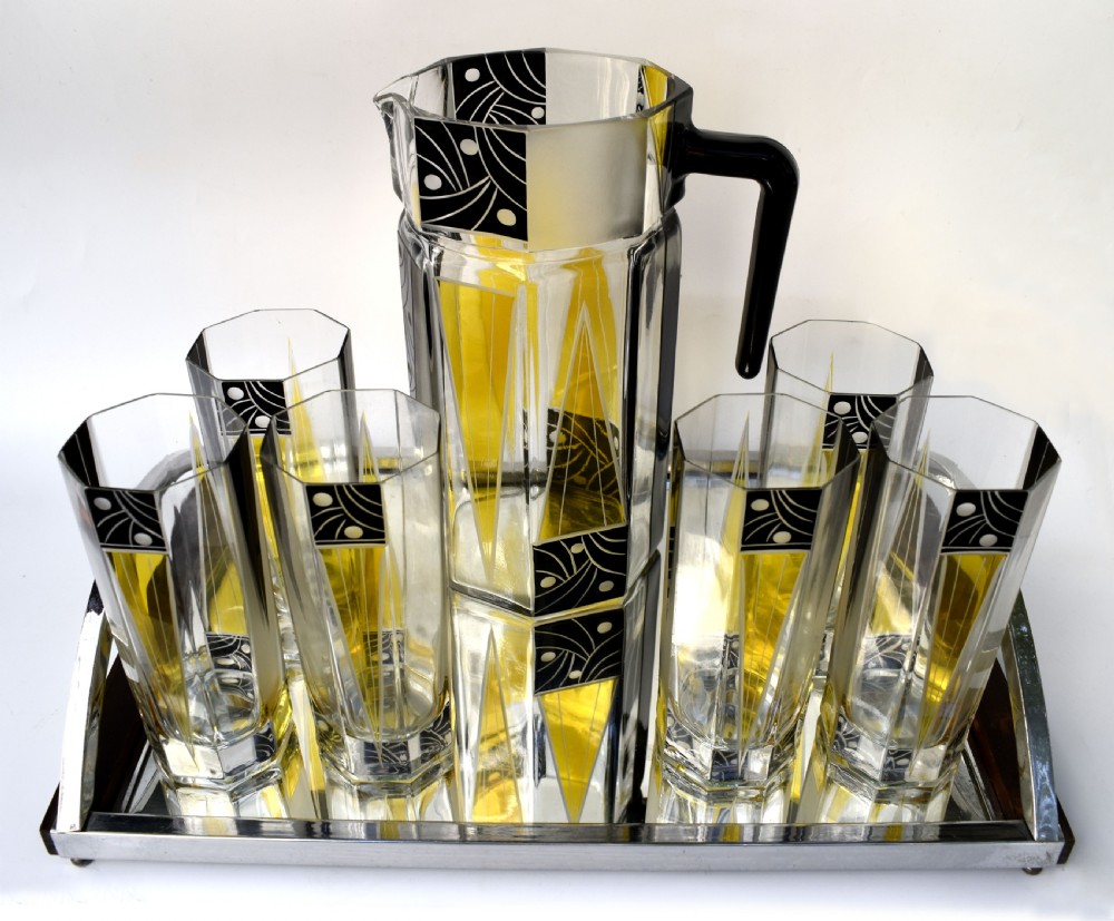 An Art Deco glass drinks set featuring a faceted glass pitcher and six matching tall glasses decorated with yellow and black geometric enamel patterns. View II