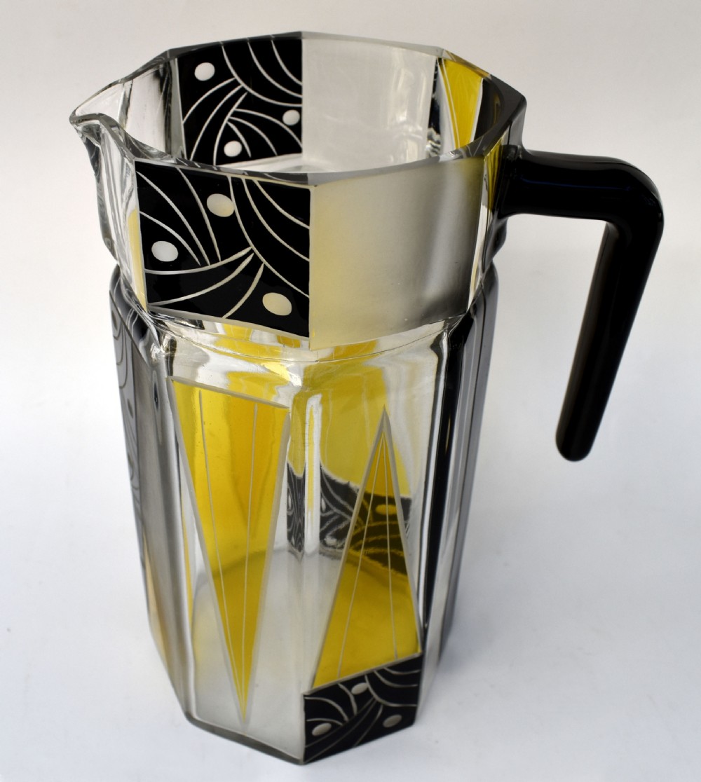 An Art Deco glass drinks set featuring a faceted glass pitcher and six matching tall glasses decorated with yellow and black geometric enamel patterns. View IV