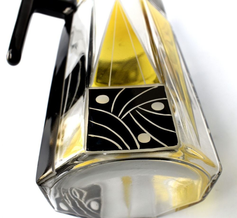 An Art Deco glass drinks set featuring a faceted glass pitcher and six matching tall glasses decorated with yellow and black geometric enamel patterns. View V