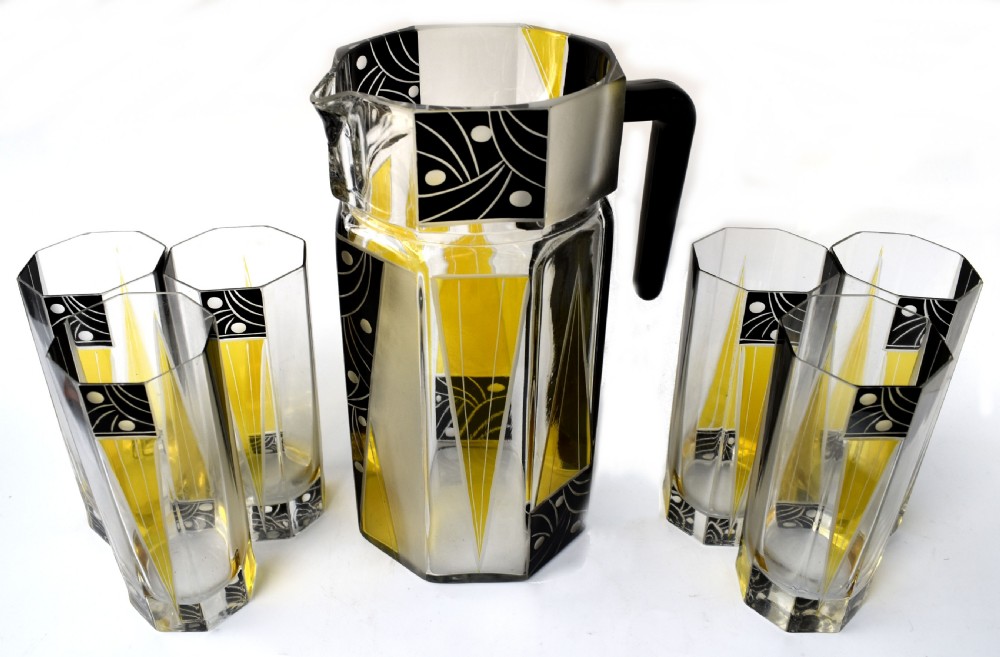 An Art Deco glass drinks set featuring a faceted glass pitcher and six matching tall glasses decorated with yellow and black geometric enamel patterns. View VII