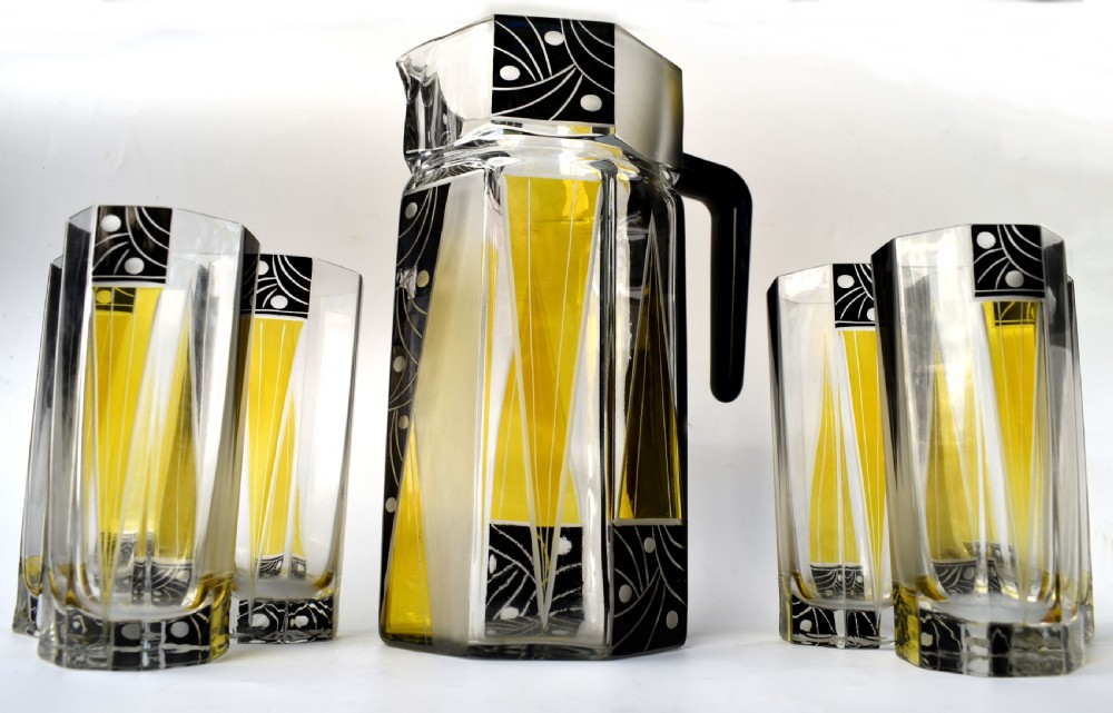 An Art Deco glass drinks set featuring a faceted glass pitcher and six matching tall glasses decorated with yellow and black geometric enamel patterns. View VIII
