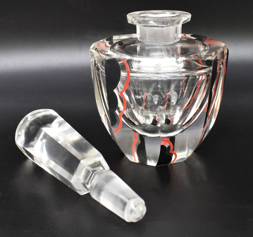 A clear cut glass Art Deco perfume bottle featuring a tall faceted stopper and black and red geometric enamel lines along the sides. View III
