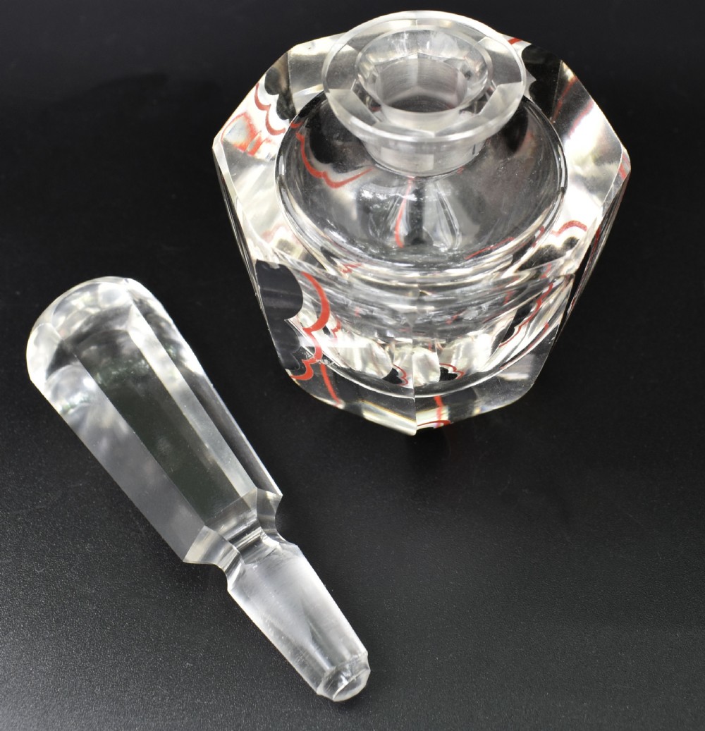 A clear cut glass Art Deco perfume bottle featuring a tall faceted stopper and black and red geometric enamel lines along the sides. View IV