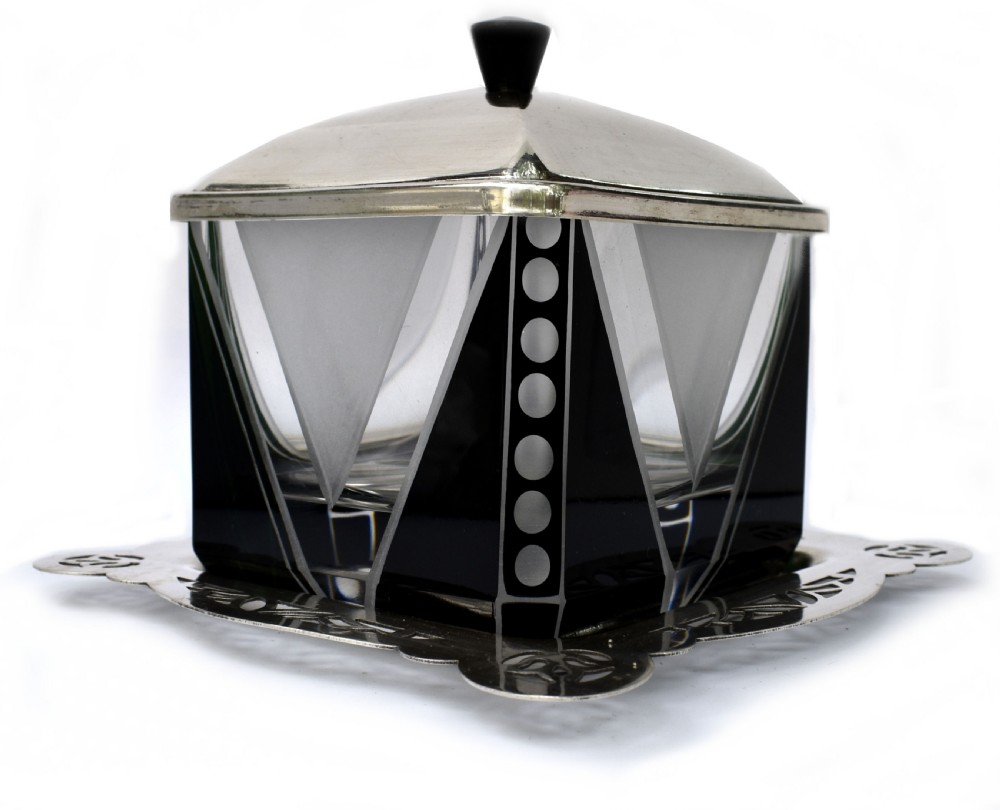 An Art Deco glass preserve dish featuring black and frosted geometric triangular motifs, topped with a silver-plated square lid and set on a pierced silver-plated tray.