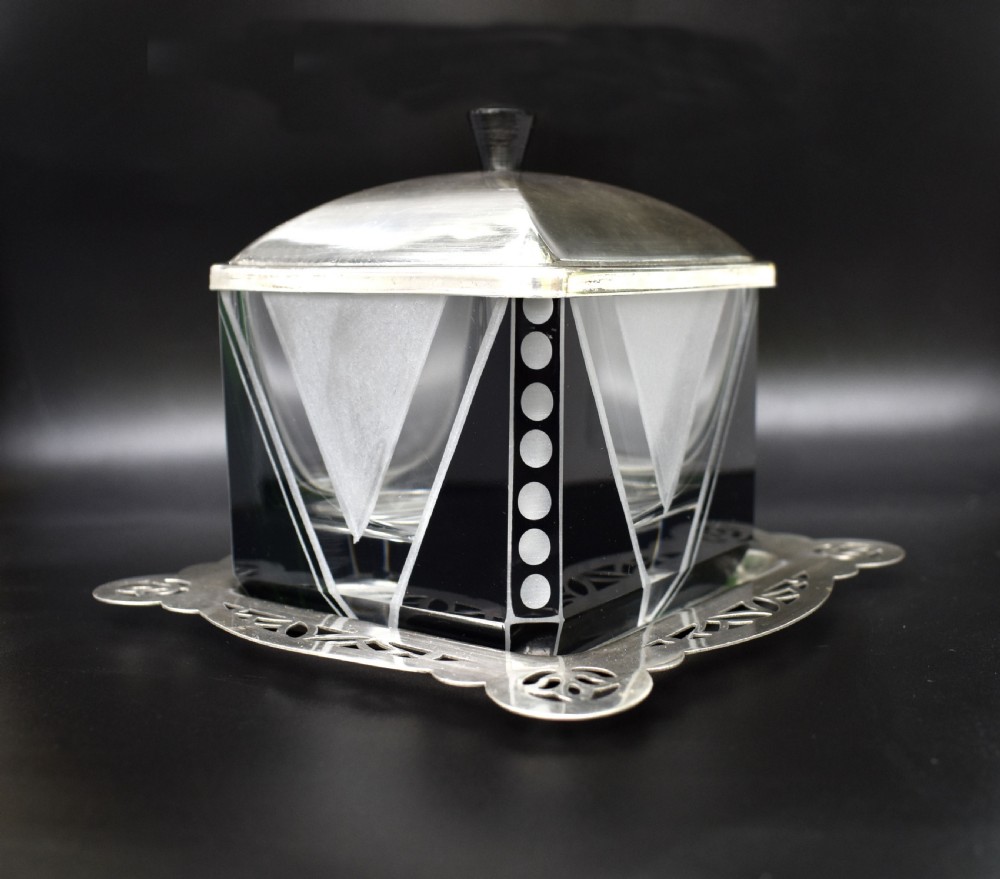 An Art Deco glass preserve dish featuring black and frosted geometric triangular motifs, topped with a silver-plated square lid and set on a pierced silver-plated tray. View II