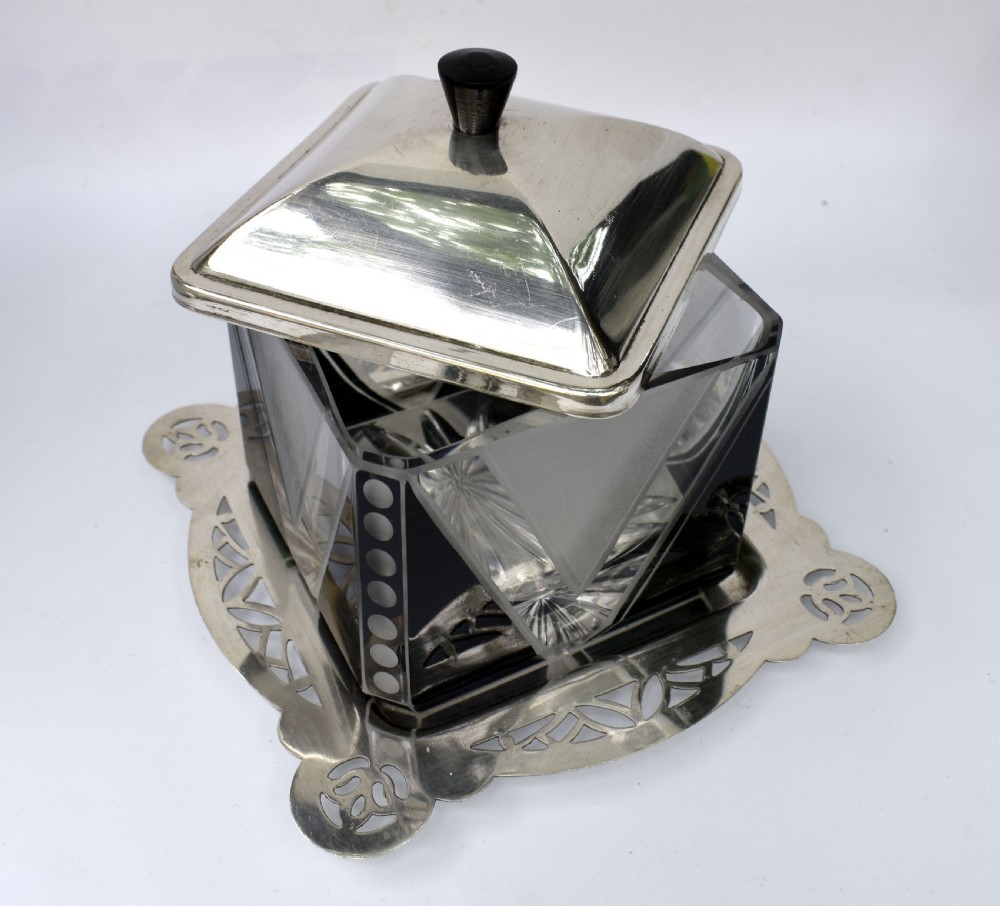 An Art Deco glass preserve dish featuring black and frosted geometric triangular motifs, topped with a silver-plated square lid and set on a pierced silver-plated tray. View IX