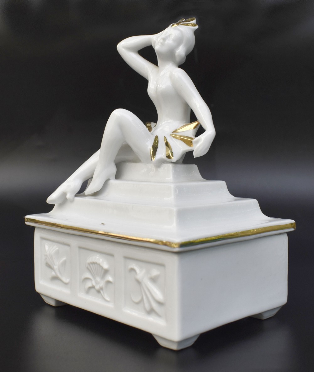 A white glazed porcelain Art Deco powder box featuring a lid topped with a seated female figure accented with gold gilding. View II