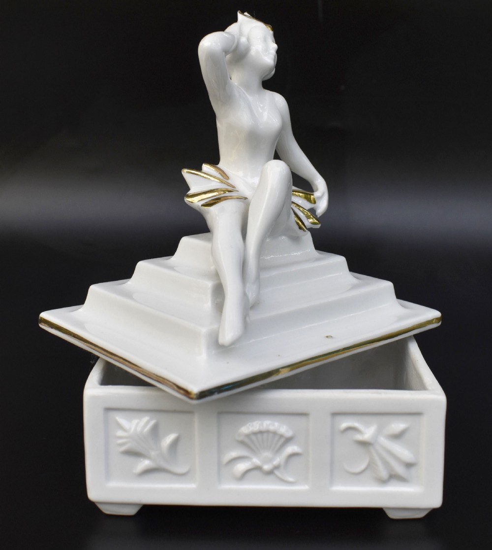 A white glazed porcelain Art Deco powder box featuring a lid topped with a seated female figure accented with gold gilding. View III