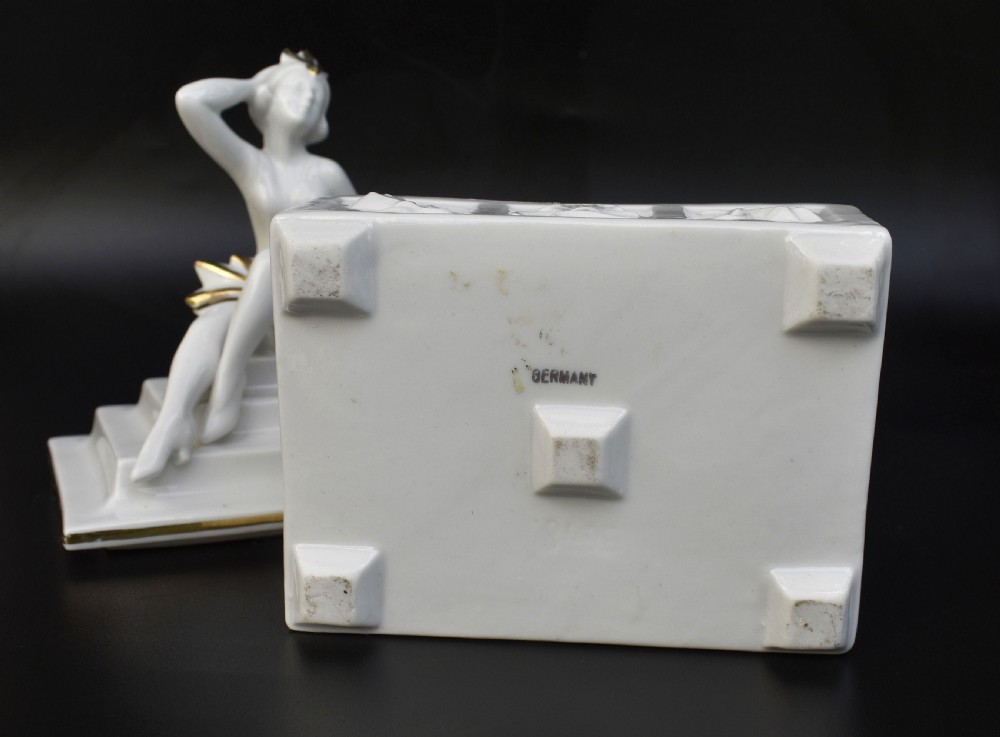 A white glazed porcelain Art Deco powder box featuring a lid topped with a seated female figure accented with gold gilding. View IV