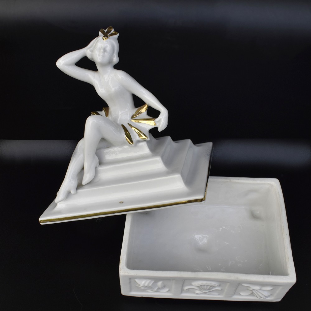 A white glazed porcelain Art Deco powder box featuring a lid topped with a seated female figure accented with gold gilding. View V