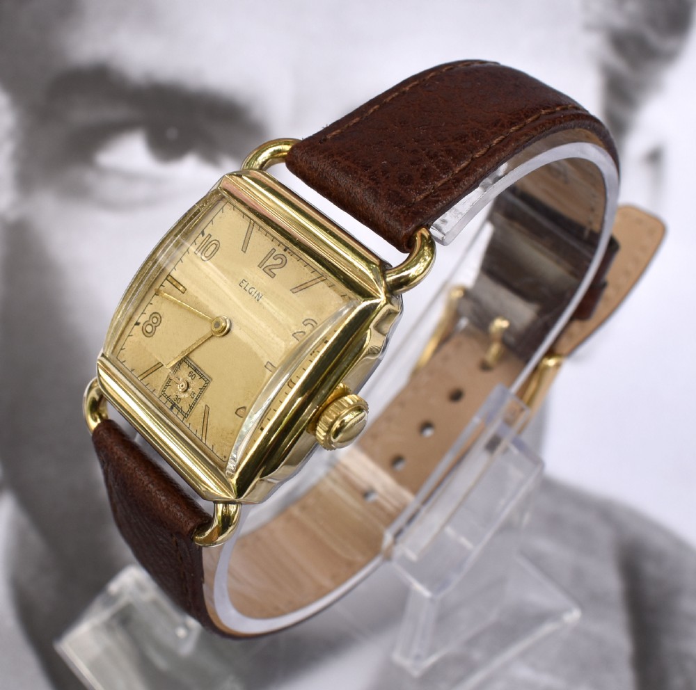 A square gold-filled vintage Elgin gents wristwatch with a champagne dial, gold Arabic numerals, sub-seconds dial, and a dark brown leather strap. View IV