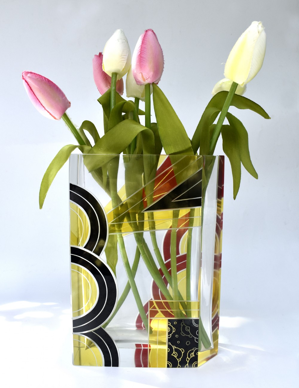 A rectangular clear glass Art Deco vase decorated with etched patterns and enamelled geometric shapes in black, yellow, and red.