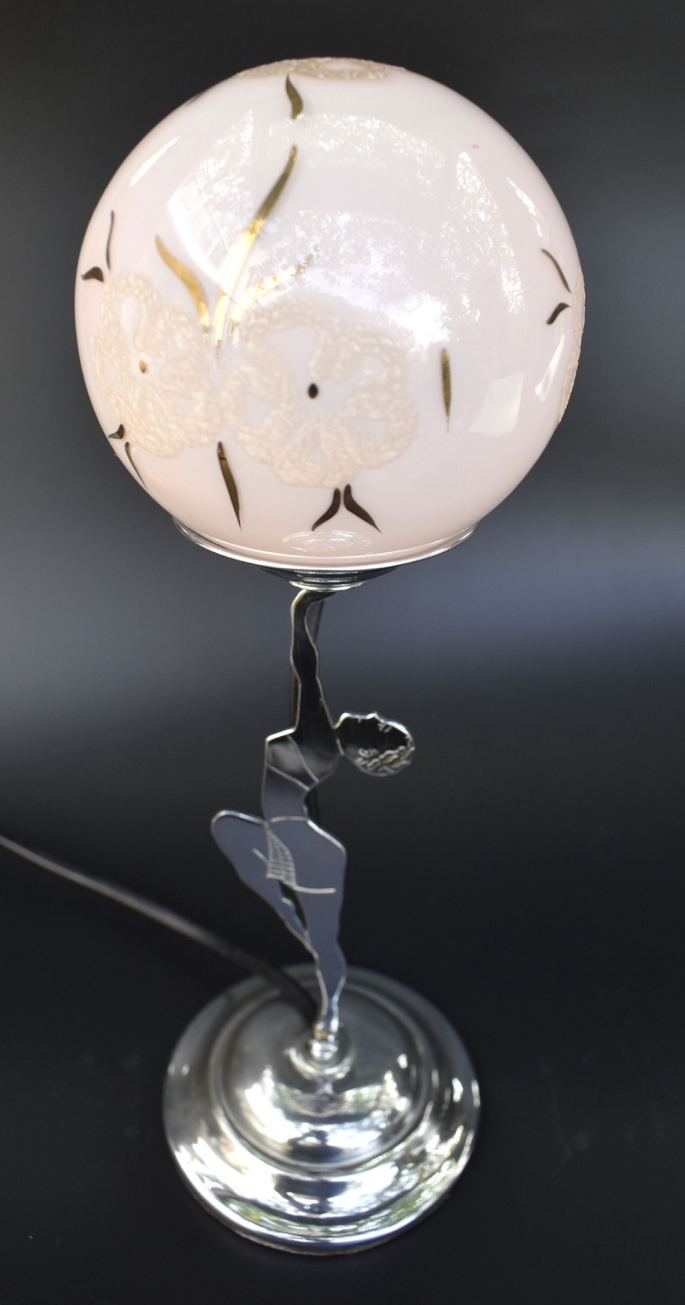An Art Deco chrome table lamp featuring a stylised female dancer figure supporting a spherical frosted glass shade with gilded detail. View II