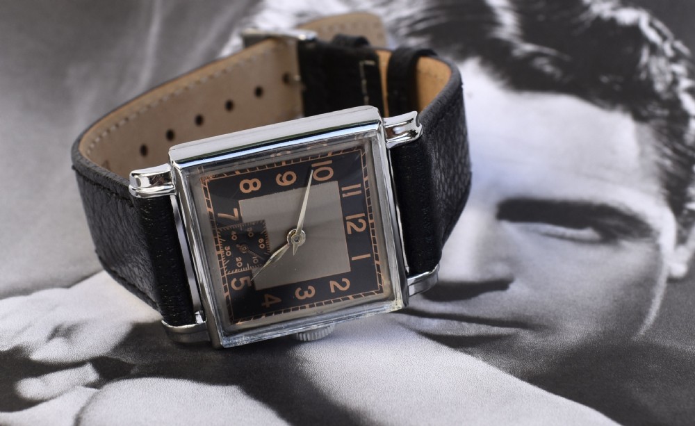 An Art Deco gentlemens wristwatch circa 1935 featuring a rectangular silver-toned case, a black two-tone dial with metallic Arabic numerals, a subdial at six oclock, and a black leather strap. View VII