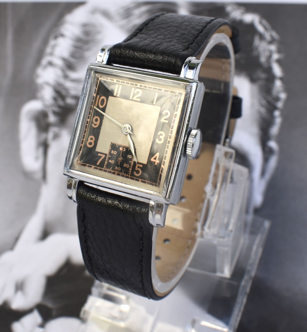 An Art Deco gentlemens wristwatch circa 1935 featuring a rectangular silver-toned case, a black two-tone dial with metallic Arabic numerals, a subdial at six oclock, and a black leather strap. View VIII