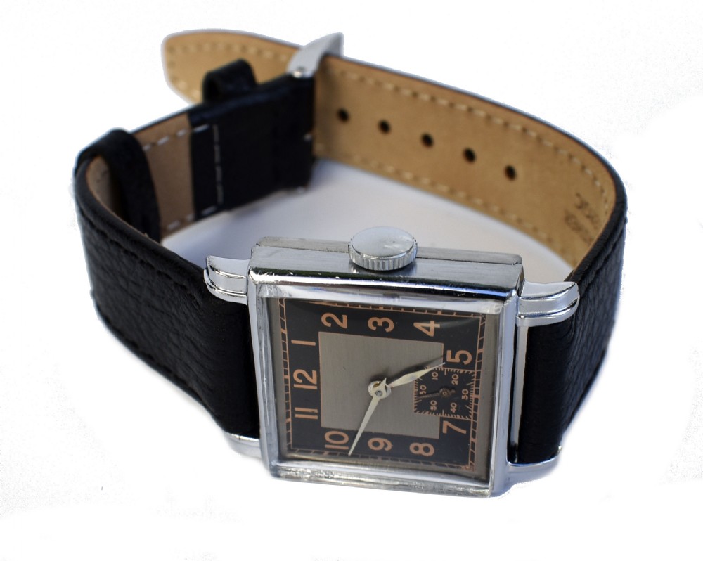 An Art Deco gentlemens wristwatch circa 1935 featuring a rectangular silver-toned case, a black two-tone dial with metallic Arabic numerals, a subdial at six oclock, and a black leather strap. View IX