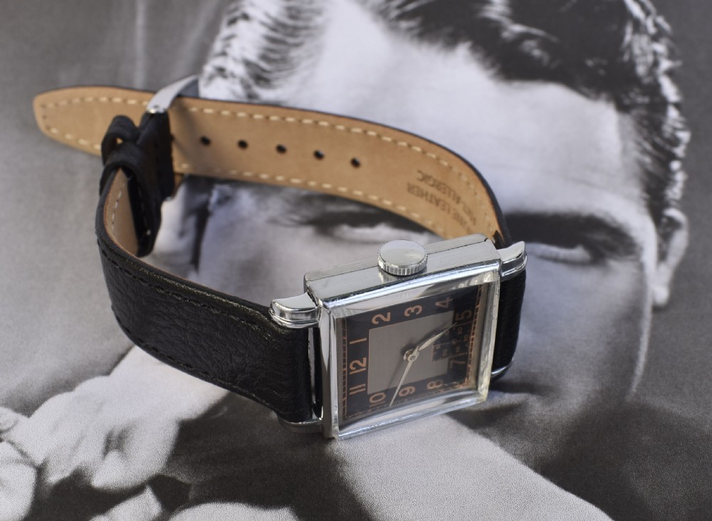 An Art Deco gentlemens wristwatch circa 1935 featuring a rectangular silver-toned case, a black two-tone dial with metallic Arabic numerals, a subdial at six oclock, and a black leather strap. View XIII