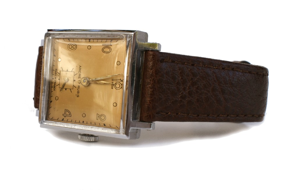 An Art Deco gents mechanical wristwatch featuring a square silver-toned case, cream dial with Arabic numerals, and a brown leather strap. View V