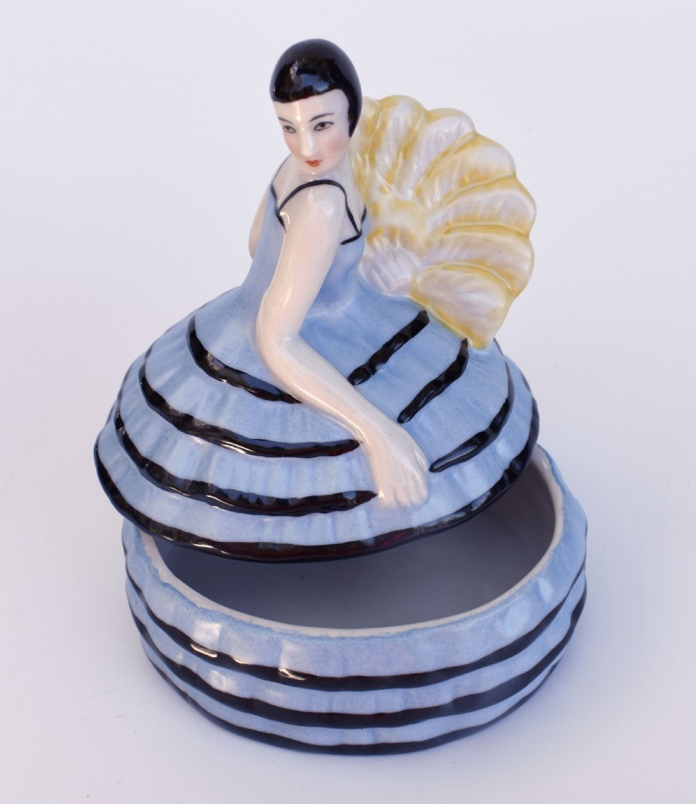 An Art Deco glazed ceramic powder box depicting a female half doll with bobbed black hair and a tiered blue ruffled dress. View V