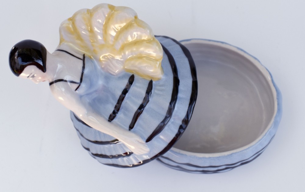An Art Deco glazed ceramic powder box depicting a female half doll with bobbed black hair and a tiered blue ruffled dress. View VII