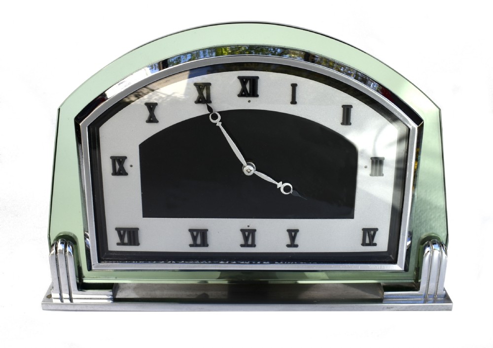 An Art Deco arched green glass mantel clock featuring a chrome frame and black Roman numerals on a two-tone dial.