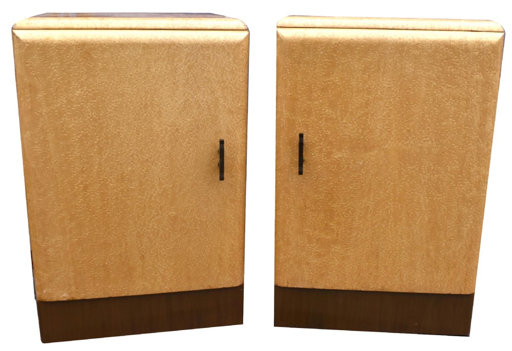 A matching pair of 1930s Art Deco bedside cabinets crafted from light blonde maple veneer with dark brown plinth bases and dark vertical door handles.