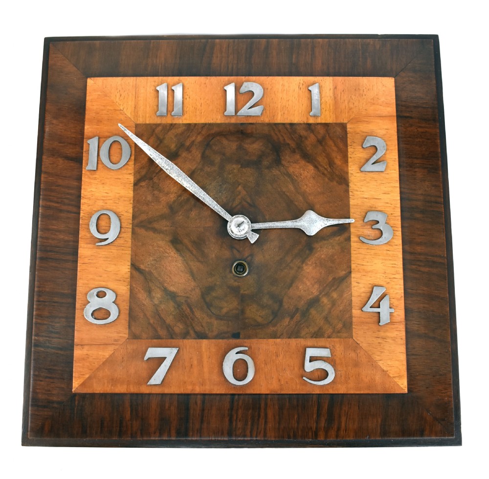 Square Art Deco walnut wall clock featuring layered wood veneers, stylized metal numerals, and metal clock hands.