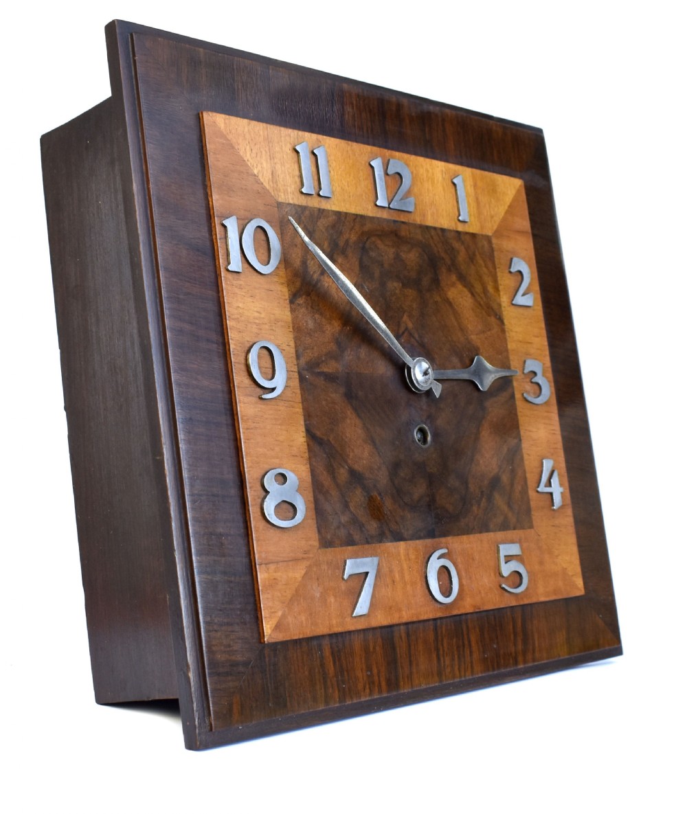 Square Art Deco walnut wall clock featuring layered wood veneers, stylized metal numerals, and metal clock hands. View III