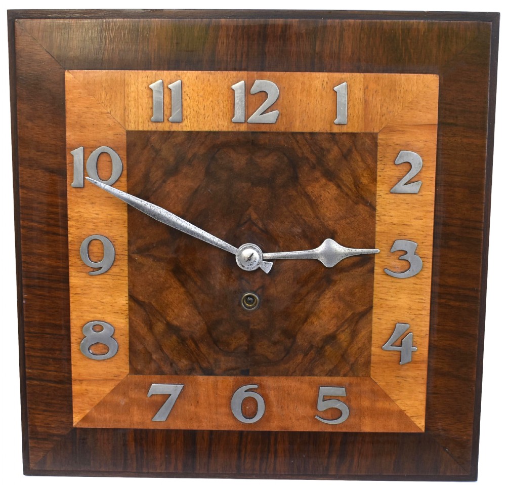 Square Art Deco walnut wall clock featuring layered wood veneers, stylized metal numerals, and metal clock hands. View XI