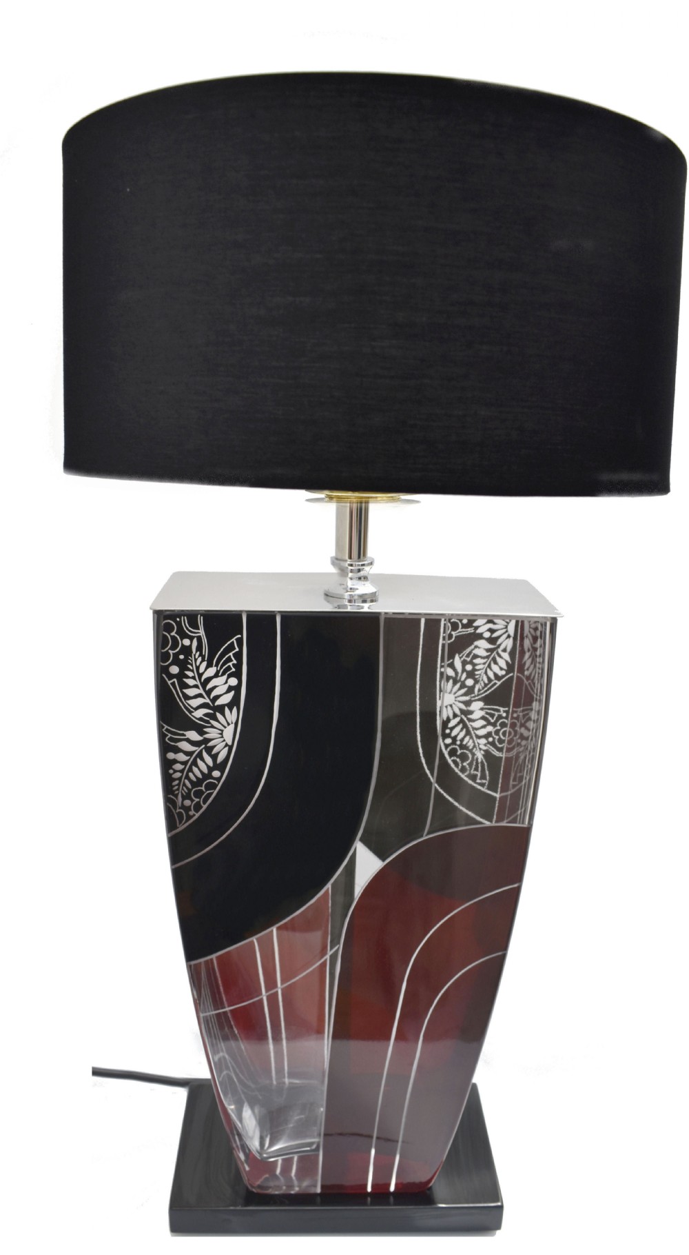 An Art Deco table lamp featuring a tapered rectangular glass base with geometric black, red, and etched foliage designs topped with a black lampshade.