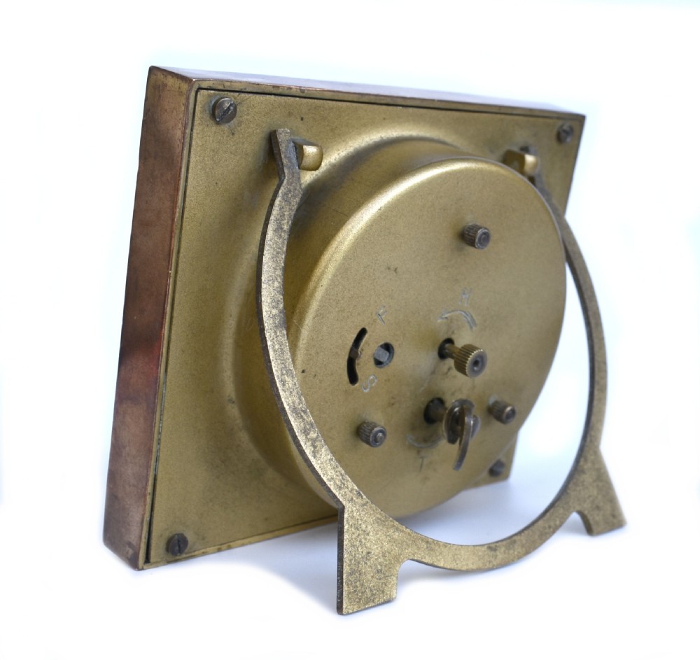 A square Art Deco clock featuring a green, white, and black chevron enamel border surrounding a geometric patterned metal dial with Arabic numerals. View III