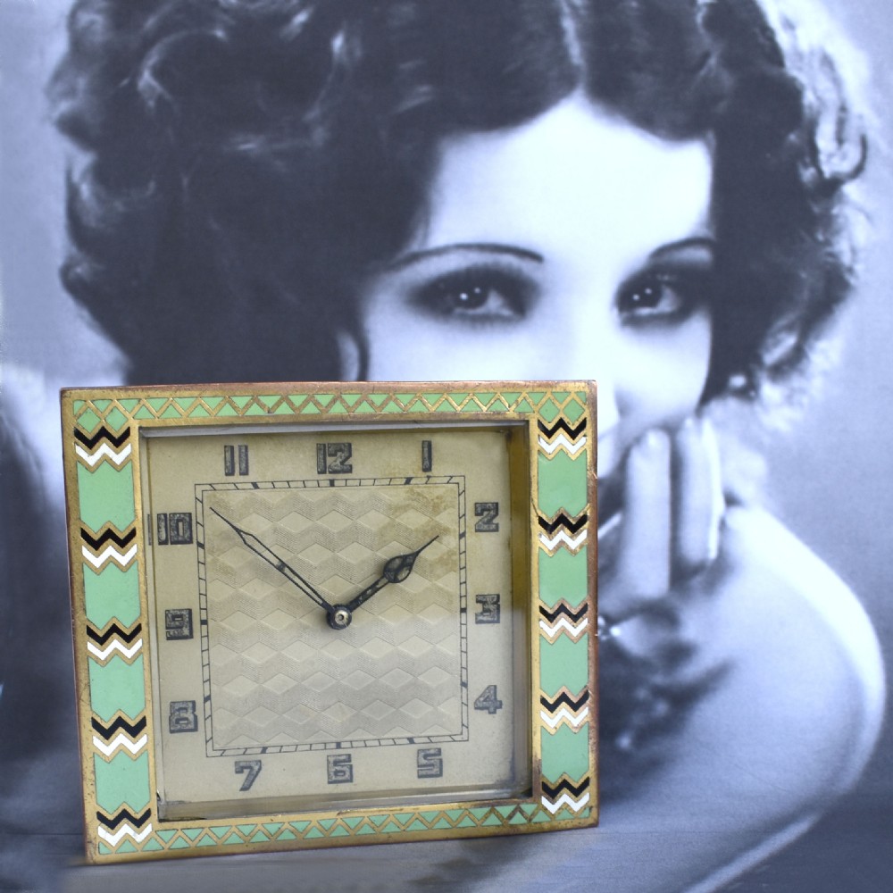 A square Art Deco clock featuring a green, white, and black chevron enamel border surrounding a geometric patterned metal dial with Arabic numerals. View IV